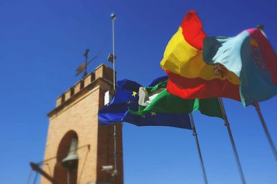 Low angle view of multi colored flags waving against bell tower