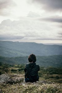 Rear view of woman sitting on landscape against mountain