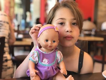 Portrait of cute girl with doll sitting on table at restaurant