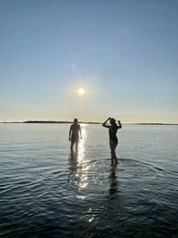 Rear view of woman standing in sea against sky during sunset