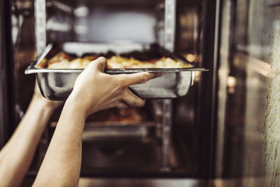 Hand av kvinnlig kock sätter in plåt i ugnen