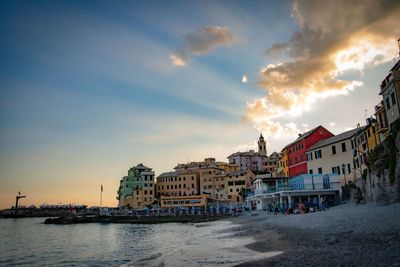 Buildings by sea against sky during sunset