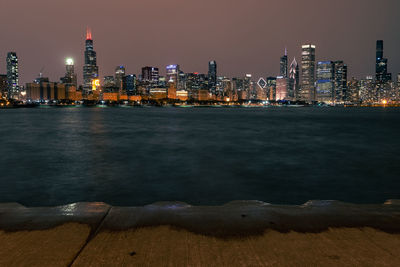 Illuminated city by sea against sky at night