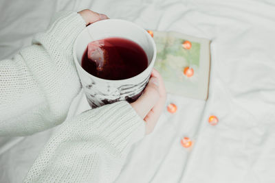 Cropped hands of woman holding drink on bed at home