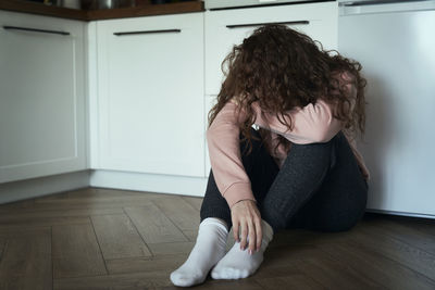 Side view of young woman sitting on hardwood floor at home