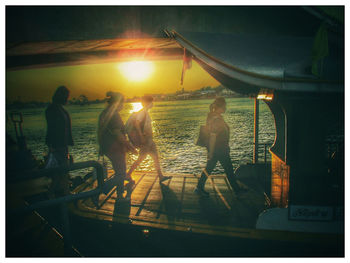 People standing by sea against sky during sunset