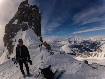 Mature man with skis standing on snow covered mountain against sky