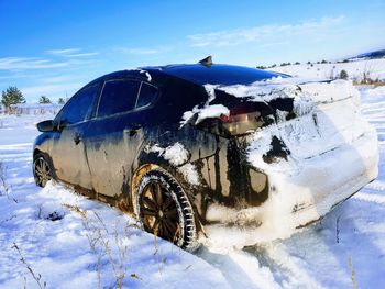 Abandoned car on snow covered field against sky