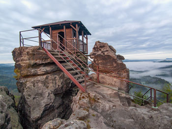 Tourist shelter or hut on rock by misty valley against sky