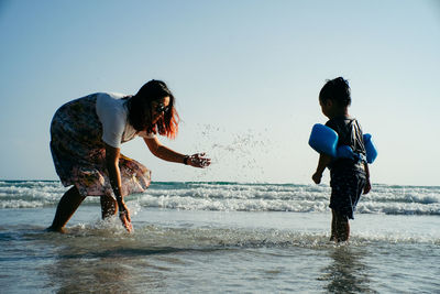 Playful mother and son at beach against clear sky