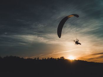 Silhouette person paragliding against sky during sunset