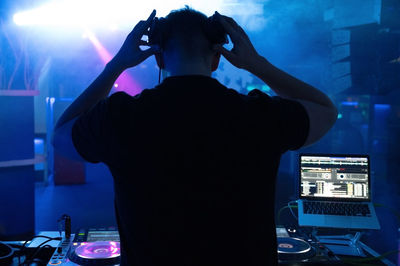 Rear view of dj playing music at night club