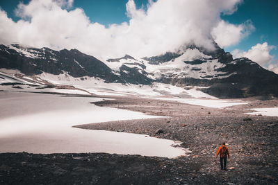 Rear view of man standing on rocks against snowcapped mountains and sky