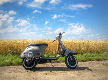 Motor scooter parked on field against sky