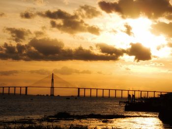 Silhouette bridge over sea against sky during sunset