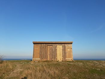 Built structure on field by sea against clear blue sky