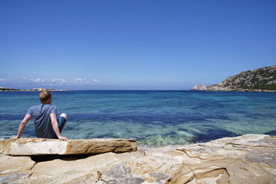 Woman on rock by sea against clear blue sky