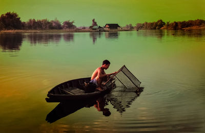 Rear view of man on boat in lake against sky