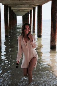 Portrait of young woman standing in sea below pier