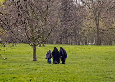 Rear view of people walking on grassy field