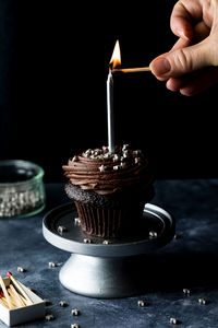 A hand lighting a candle on a chocolate cupcake, against a black background.