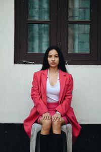 Portrait of young woman standing against wall