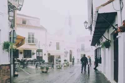 People walking on street amidst buildings during rainy season