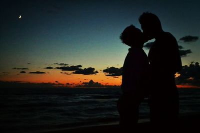 Silhouette of people standing on beach at sunset