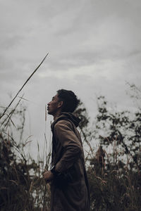 Side view of young man looking away on field against sky