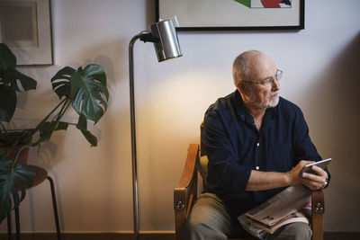 Senior man looking away while holding smart phone at home