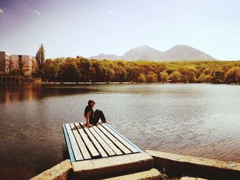 Man sitting on lake against mountains