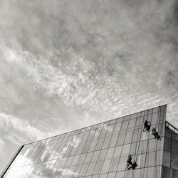 Low angle view of people working on building against sky