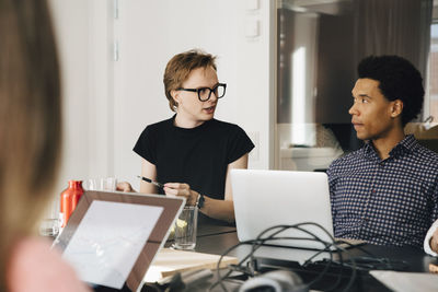 Businessman looking young genderblend professional during discussion in board room