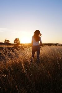 Rear view of teenage girl standing on grassy field against sky during sunset