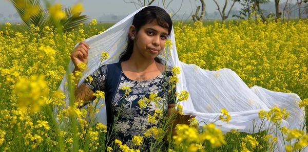 Beautiful woman standing on field by yellow flowering plants