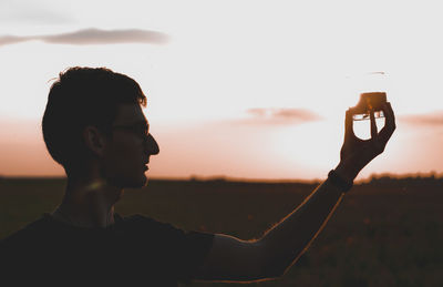 Portrait of young man using smart phone against sky during sunset