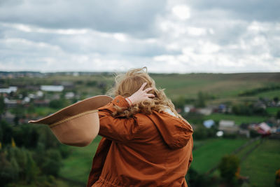 Rear view of woman with hand in hair by landscape against cloudy sky