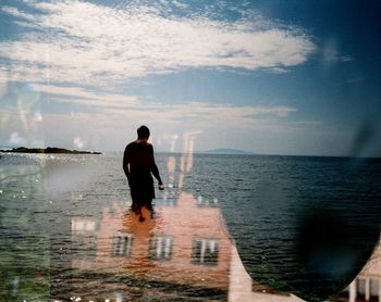 Rear view of man standing at beach against sky