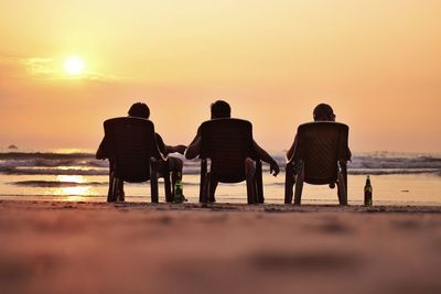 Rear view of people sitting on chair at beach during sunset