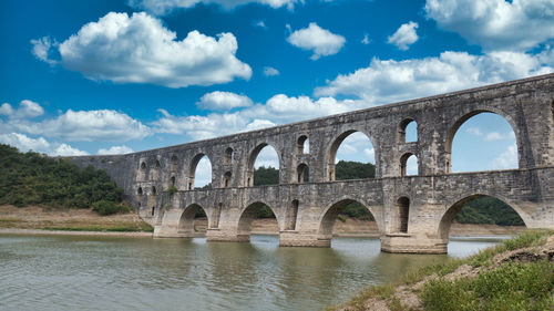Arch bridge over river against cloudy sky