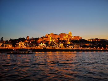 River by illuminated buildings against sky at dusk