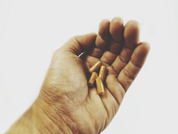 Close-up of hand holding cigarette over white background
