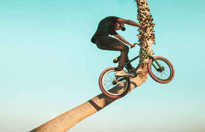 Low angle view of man with bicycle performing stunt against clear sky