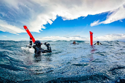 Scuba divers on sea against cloudy sky