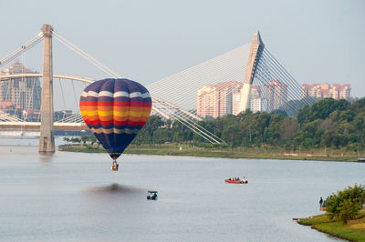 Hot air balloons over river against bridge