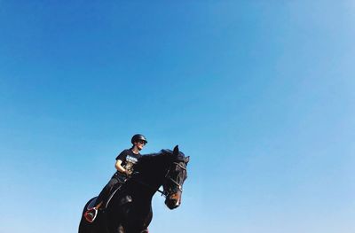 Low angle view of people riding horse against blue sky