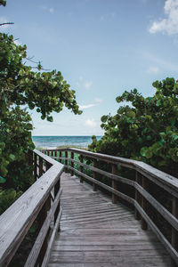 Wooden bridge over calm sea against sky