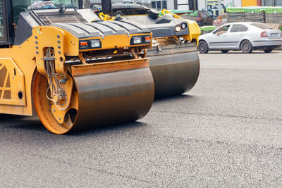 Road rollers compacting fresh asphalt on the carriageway against the backdrop of a city street.
