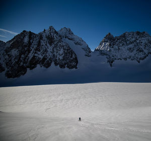 Mid distance view of person walking on snow covered landscape against blue sky