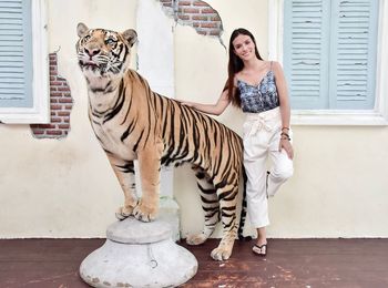 Portrait of young woman standing by artificial tiger against building